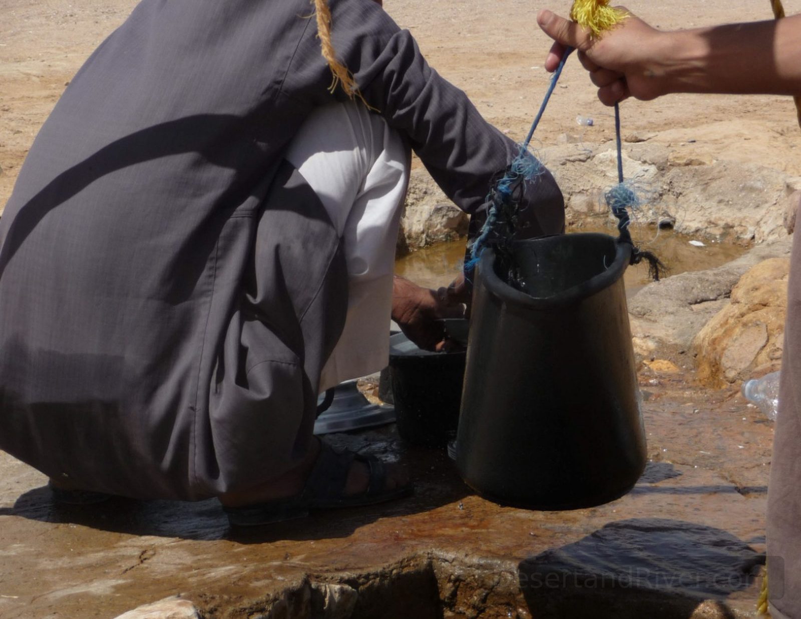 Bir Safra well in South Sinai, with a man drawing water from a small desert spring opening in a sandstone plain.