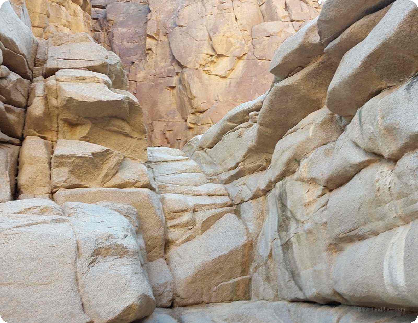Sunlit granite canyon walls in Wadi El Rum, South Sinai, with smooth boulders and warm rock layers forming a narrow desert passage.